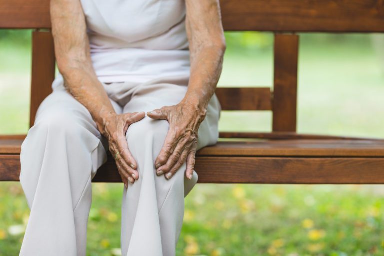 Senior woman sitting on bench, holding her painful knee